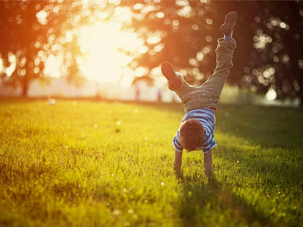 Little boy doing handstand in yard in summer