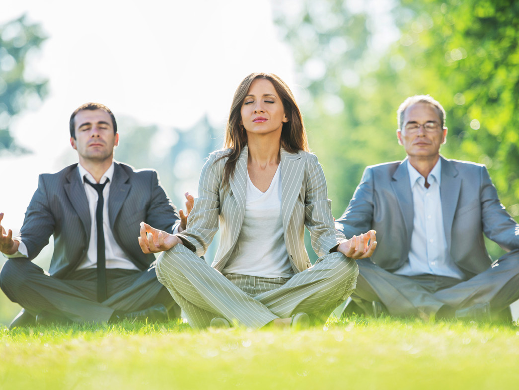 Three people in business suits doing yoga in the grass