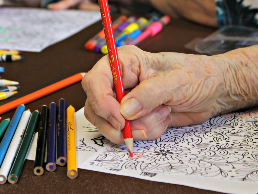 Person coloring in coloring page with red colored pencil