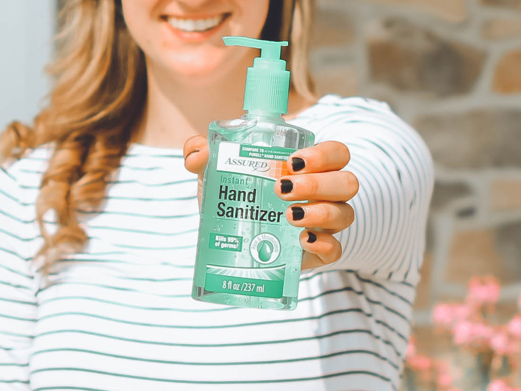 Woman smiling and holding out bottle of hand sanitizer
