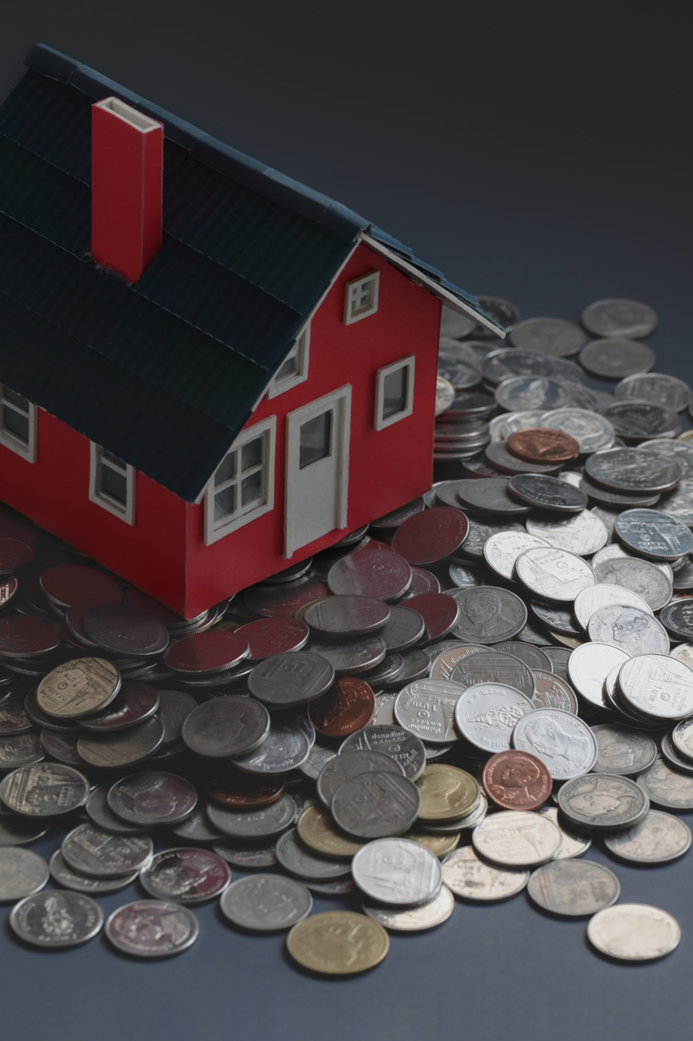 miniature red home with pile of coins