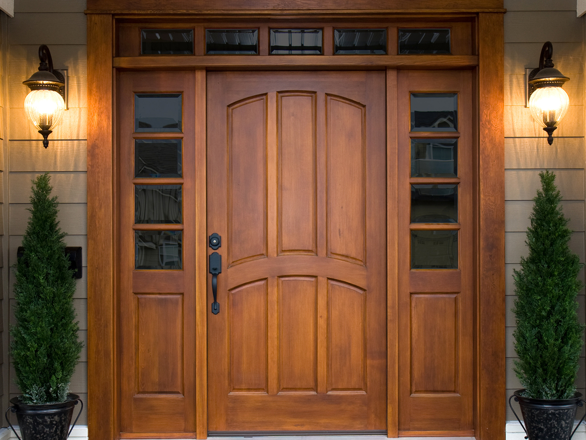 large wooden front door with hanging lights and topiaries