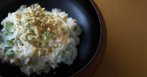 japanese potato salad in black bowl with cracked egg