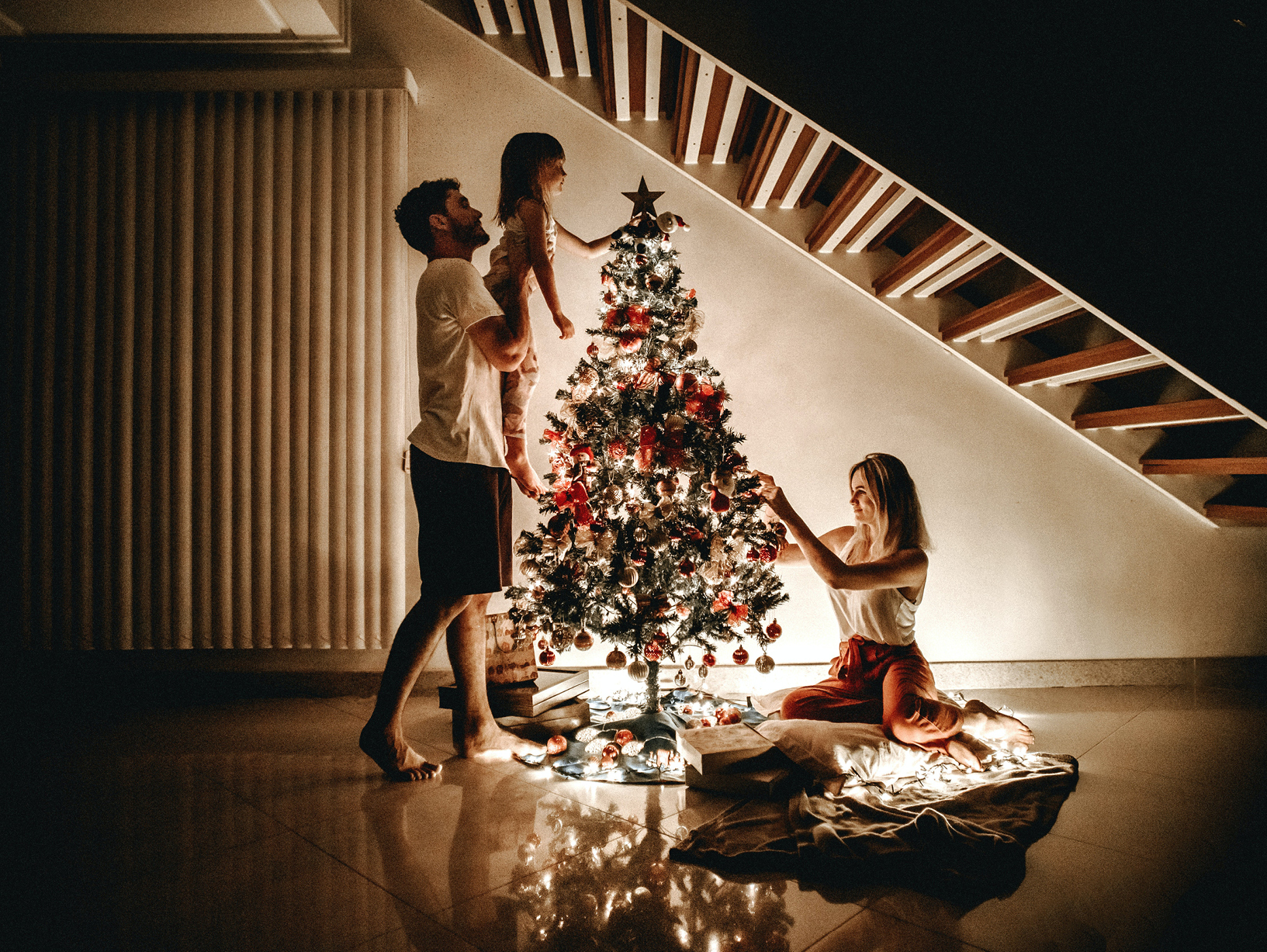 family setting up a christmas tree by staircase
