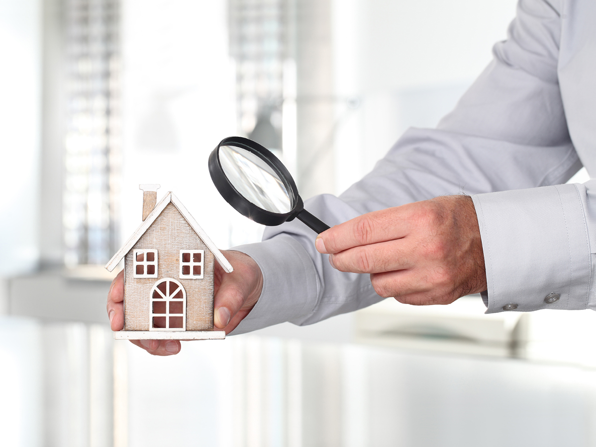 person holding magnifrying glass up to minature home